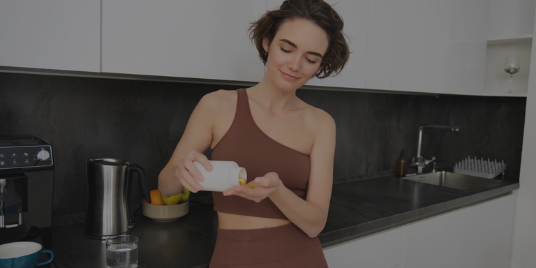 Woman pouring supplement capsules into her hand in a kitchen.